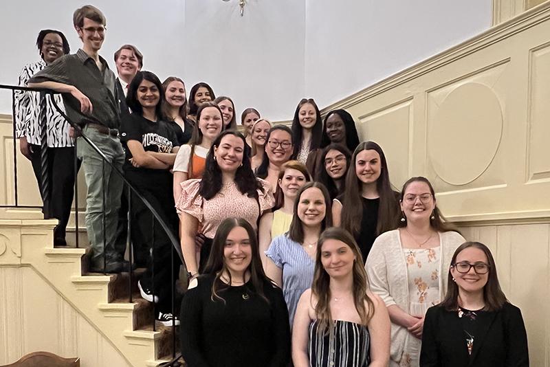 The 2023 Class of Washington College's Chapter of Phi Beta Kappa smile for a portrait from the staircase in Hynson Lounge